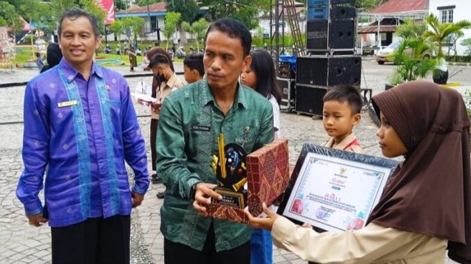 Kepala Dinas Pariwisata Pemuda dan Olahraga Kota Sawahlunto, disaksikan Kepala Dinas Pendidikan saat menyerahkan Piala pada Pemenang Juara 1 Melukis Payung Kote